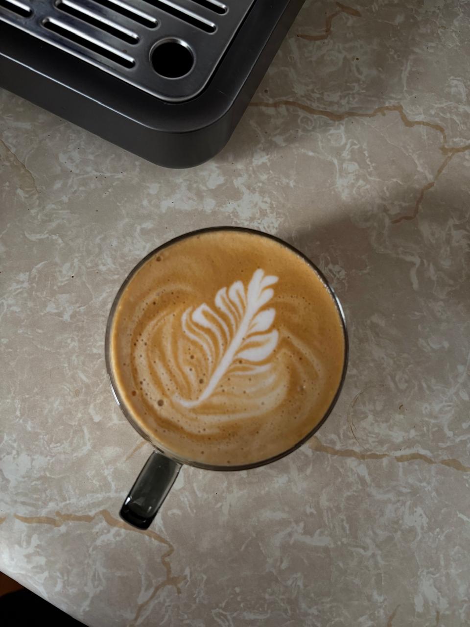 Latte con arte de hoja junto a una máquina de espresso